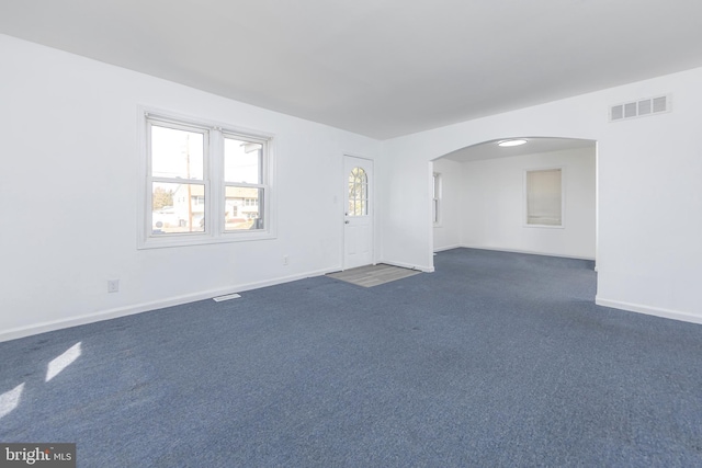 unfurnished room featuring dark colored carpet, visible vents, arched walkways, and baseboards