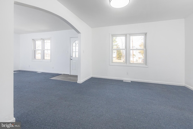 spare room featuring arched walkways, baseboards, and dark colored carpet