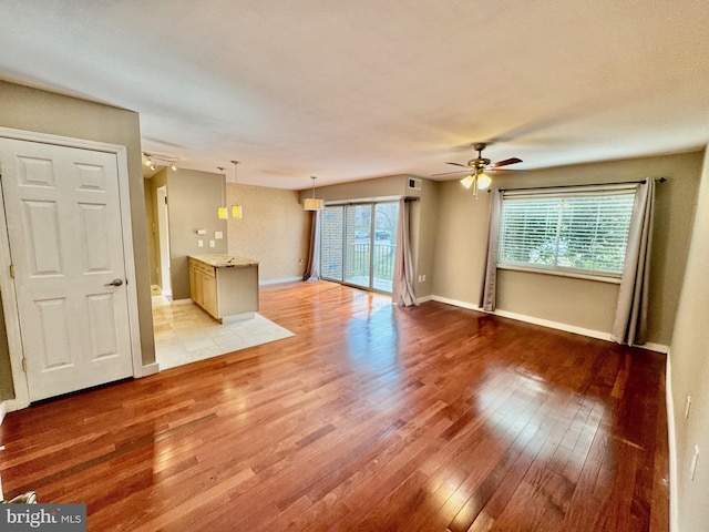 unfurnished living room featuring light wood-style flooring, baseboards, and a ceiling fan