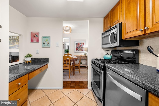 kitchen featuring backsplash, built in desk, brown cabinets, appliances with stainless steel finishes, and light tile patterned flooring