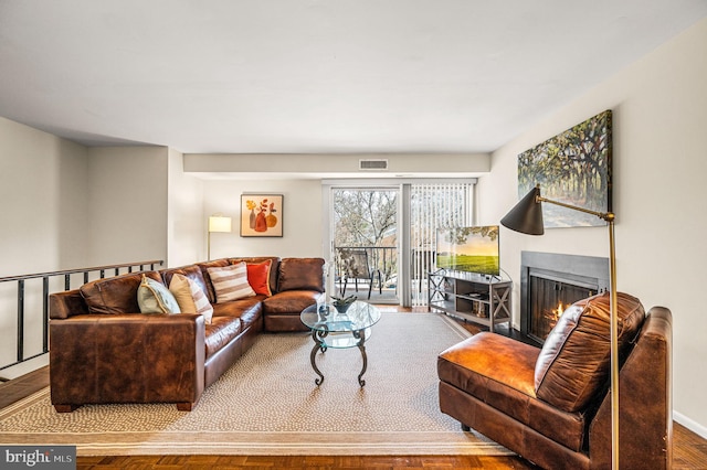 living room with wood finished floors, visible vents, a warm lit fireplace, and baseboards