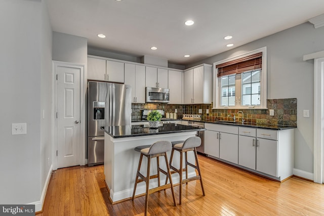 kitchen with a sink, decorative backsplash, light wood-style floors, and stainless steel appliances