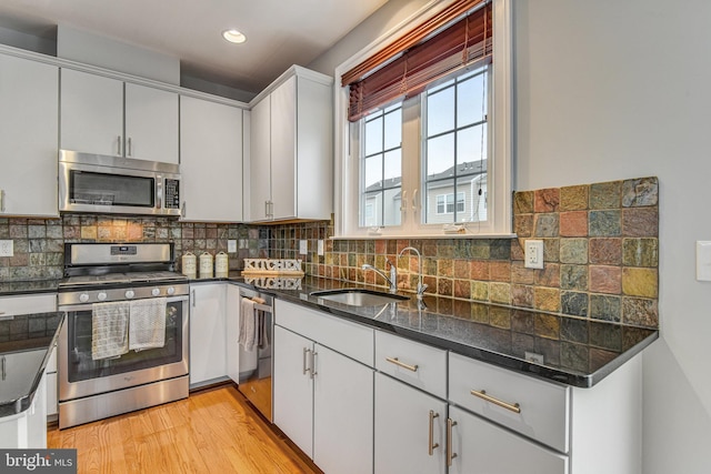 kitchen featuring decorative backsplash, appliances with stainless steel finishes, light wood-style floors, white cabinetry, and a sink