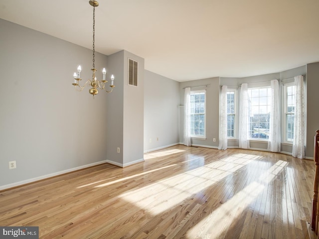 unfurnished room with hardwood / wood-style flooring, baseboards, visible vents, and a chandelier