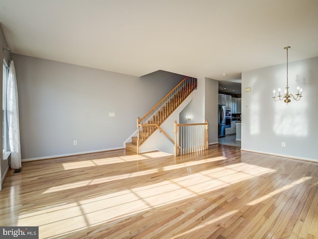 unfurnished living room with light wood finished floors, baseboards, stairs, and an inviting chandelier