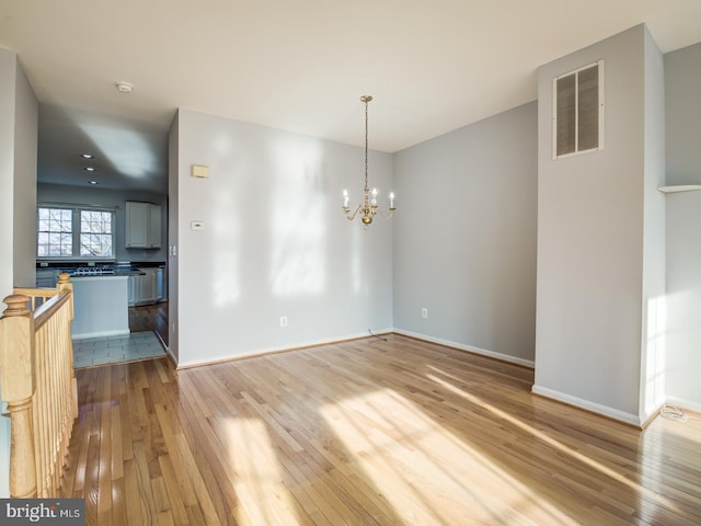 unfurnished dining area with light wood finished floors, a chandelier, baseboards, and visible vents