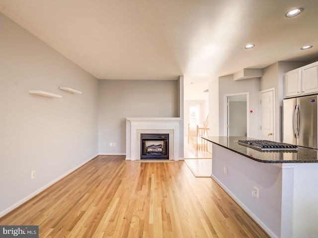 unfurnished living room with recessed lighting, light wood-style floors, baseboards, and a fireplace with flush hearth