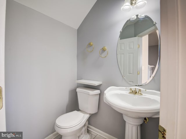 half bath featuring vaulted ceiling, toilet, and baseboards