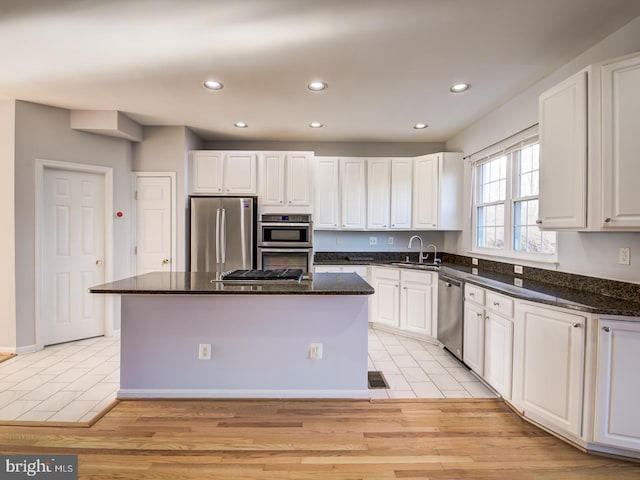 kitchen featuring a kitchen island, a sink, light wood-style floors, appliances with stainless steel finishes, and white cabinetry