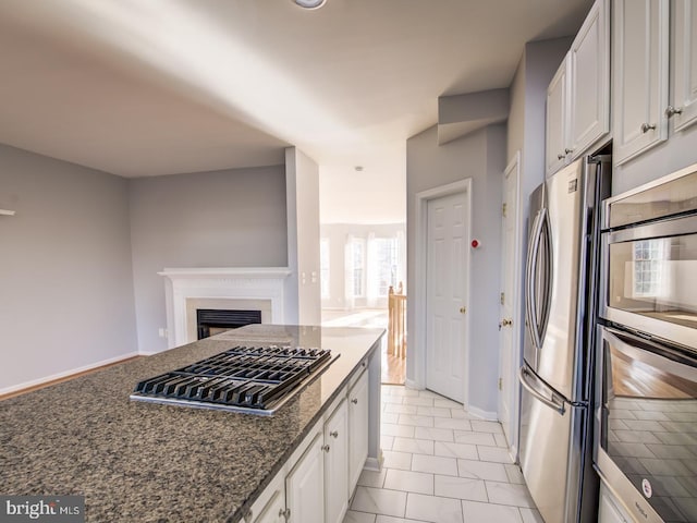 kitchen with dark stone countertops, a fireplace, stainless steel appliances, white cabinets, and open floor plan