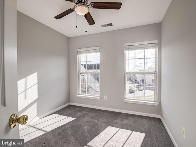 spare room featuring baseboards, visible vents, dark carpet, and ceiling fan