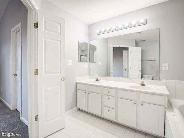 bathroom with a sink, a relaxing tiled tub, baseboards, and double vanity