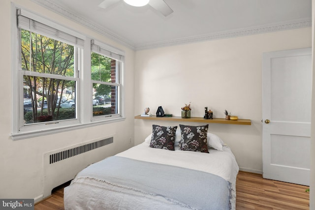 bedroom featuring baseboards, radiator, wood finished floors, and crown molding