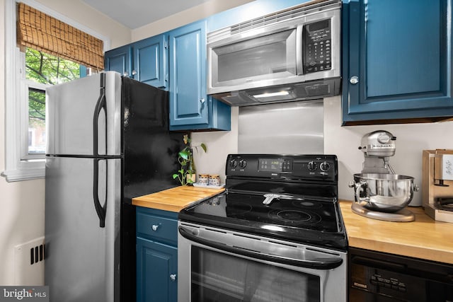 kitchen with blue cabinetry, appliances with stainless steel finishes, and butcher block counters