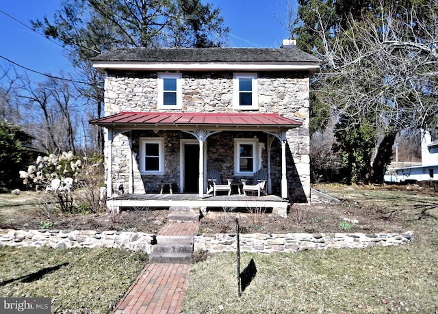 view of front facade featuring a standing seam roof, covered porch, stone siding, and metal roof