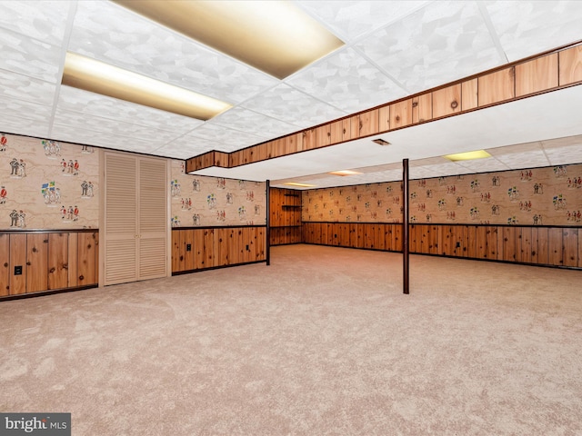 finished basement with a paneled ceiling, a wainscoted wall, carpet floors, and wallpapered walls