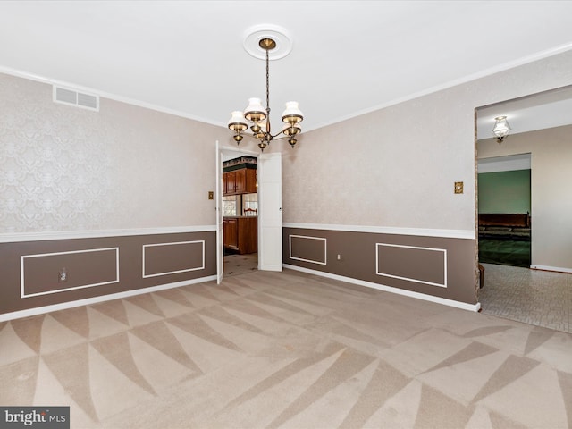 carpeted spare room featuring visible vents, a chandelier, wainscoting, and crown molding