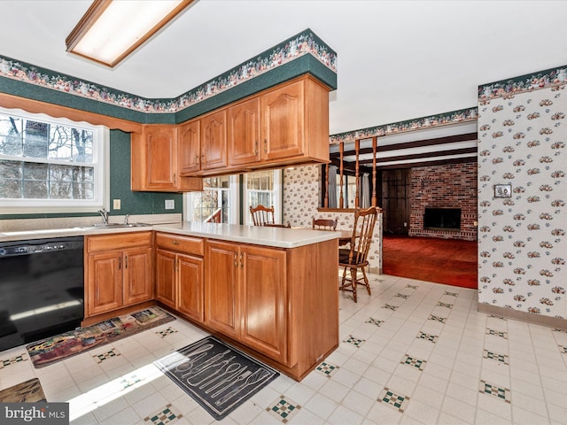 kitchen featuring a peninsula, a sink, light countertops, dishwasher, and a brick fireplace