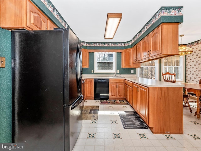 kitchen with black appliances, a peninsula, light countertops, and a sink