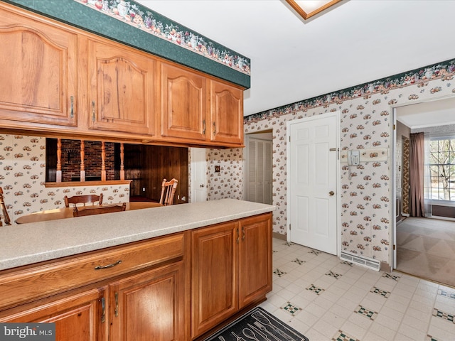 kitchen featuring brown cabinetry, wallpapered walls, and light countertops