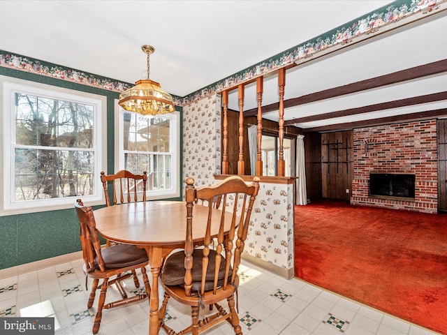 dining space with a brick fireplace, wallpapered walls, baseboards, a chandelier, and beamed ceiling