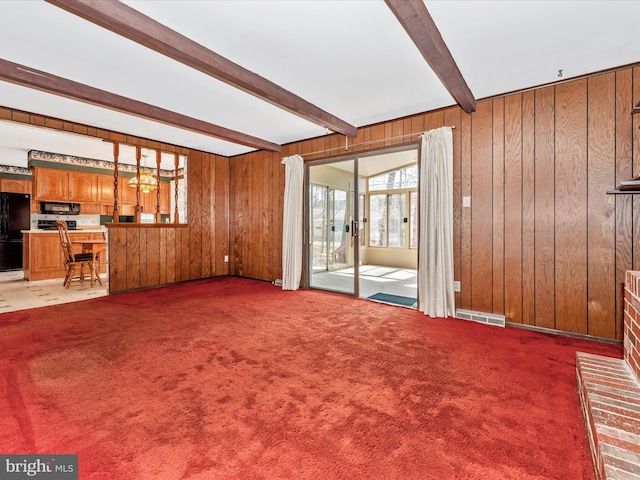 unfurnished living room featuring beamed ceiling, wooden walls, visible vents, and carpet