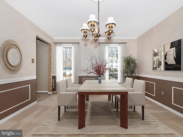 carpeted dining area with ornamental molding, a wainscoted wall, and a chandelier