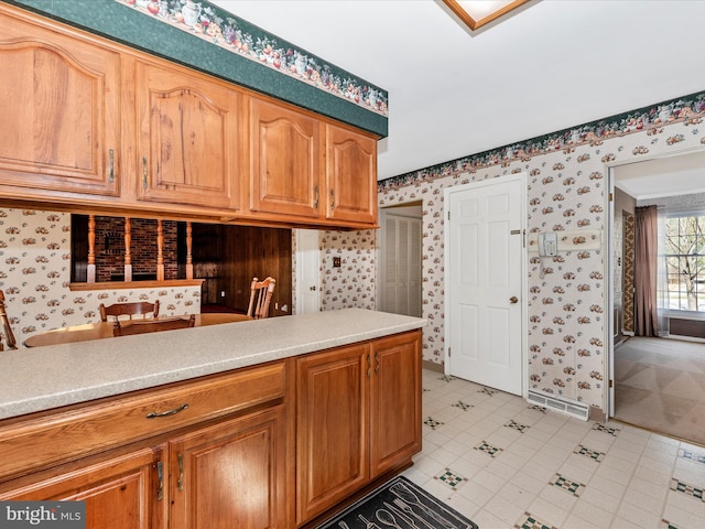 kitchen with brown cabinets, wallpapered walls, and light countertops