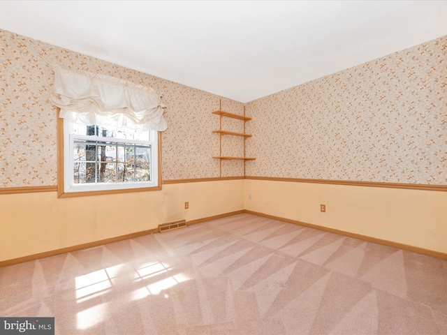 empty room featuring wallpapered walls, visible vents, and wainscoting