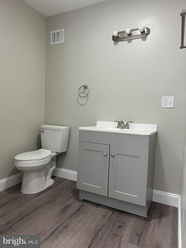 half bath featuring visible vents, vanity, baseboards, and wood finished floors