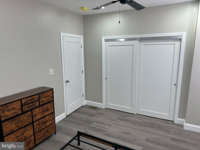 bedroom with a ceiling fan, wood finished floors, baseboards, and a closet