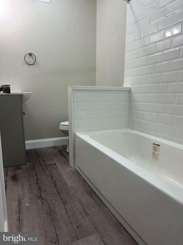 bathroom featuring baseboards, a washtub, toilet, wood finished floors, and vanity