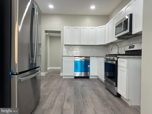 kitchen featuring light wood-type flooring, stainless steel appliances, tasteful backsplash, and white cabinets