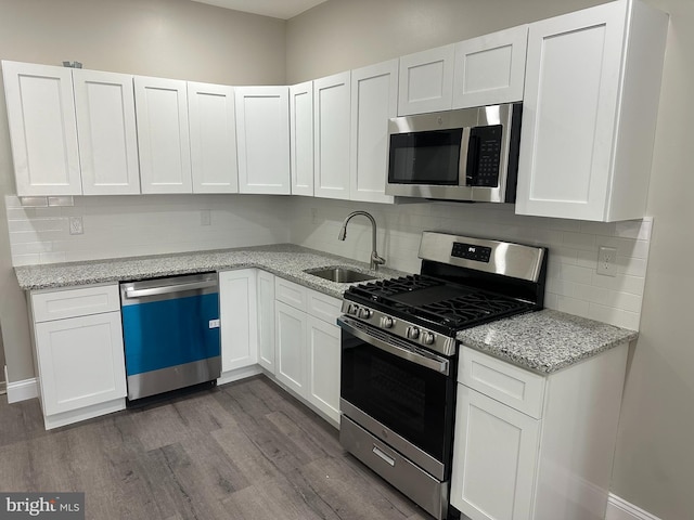 kitchen featuring a sink, light stone countertops, appliances with stainless steel finishes, white cabinets, and dark wood-style flooring