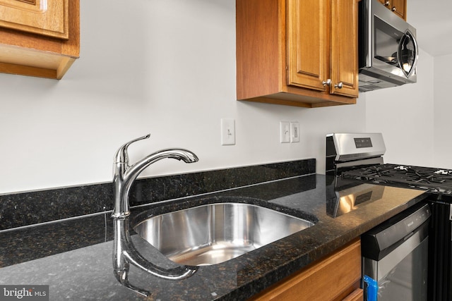 kitchen featuring a sink, dark stone counters, appliances with stainless steel finishes, and brown cabinetry