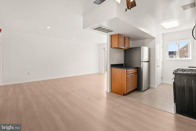 kitchen with visible vents, freestanding refrigerator, ceiling fan, range with gas cooktop, and brown cabinets