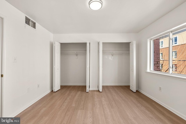 unfurnished bedroom with visible vents, multiple closets, baseboards, and light wood finished floors