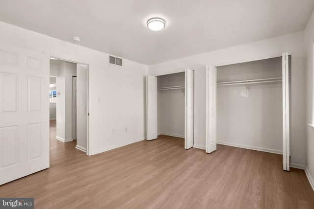 unfurnished bedroom with light wood-type flooring, baseboards, two closets, and visible vents