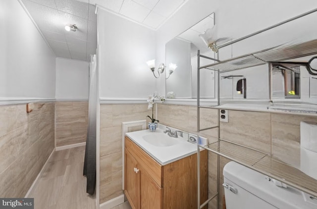 bathroom with toilet, wood finished floors, tile walls, wainscoting, and vanity