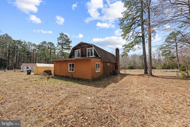 view of side of property featuring a gambrel roof, cooling unit, and a chimney