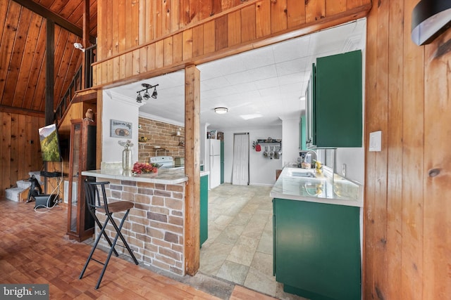 kitchen with a sink, freestanding refrigerator, wooden walls, light countertops, and green cabinetry