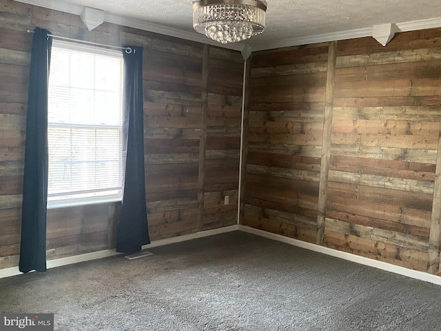 carpeted spare room featuring baseboards, wooden walls, ornamental molding, and a textured ceiling