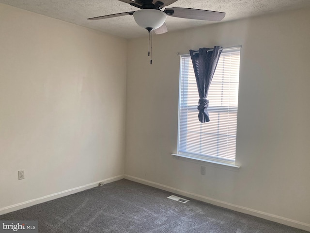 empty room with visible vents, dark carpet, a textured ceiling, and a ceiling fan