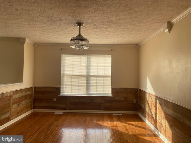 unfurnished room with ornamental molding, hardwood / wood-style flooring, a textured ceiling, wood walls, and wainscoting