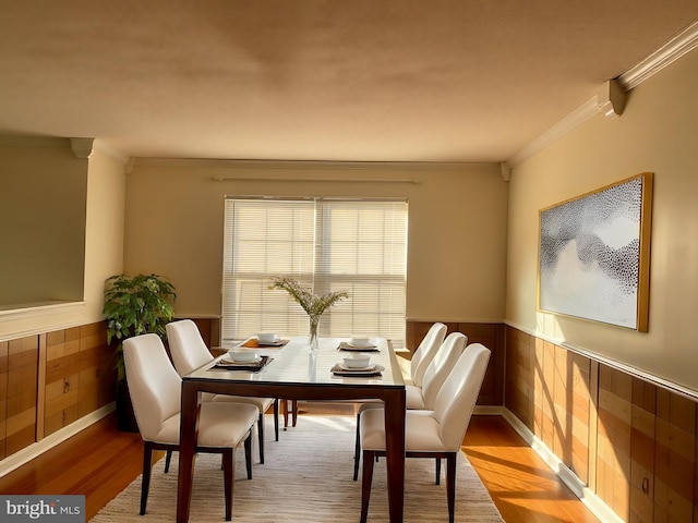 dining space featuring wooden walls, wood finished floors, wainscoting, and ornamental molding