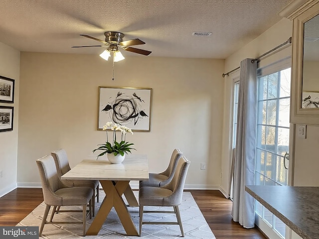 dining area with dark wood finished floors, a ceiling fan, visible vents, and baseboards