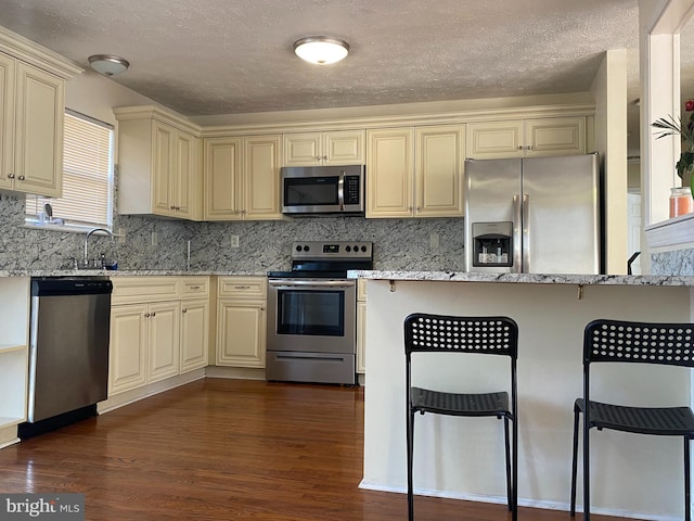 kitchen with cream cabinets, stainless steel appliances, dark wood-type flooring, and light stone countertops