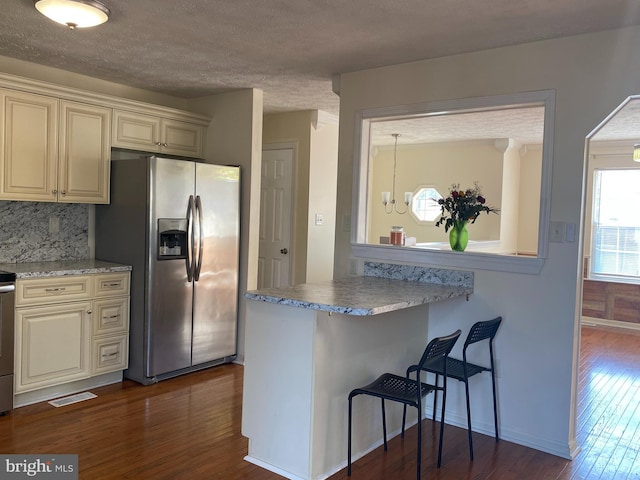 kitchen with visible vents, stainless steel fridge with ice dispenser, a breakfast bar area, dark wood-style floors, and cream cabinetry