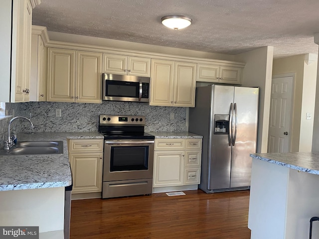 kitchen with dark wood-type flooring, light countertops, appliances with stainless steel finishes, cream cabinetry, and a sink