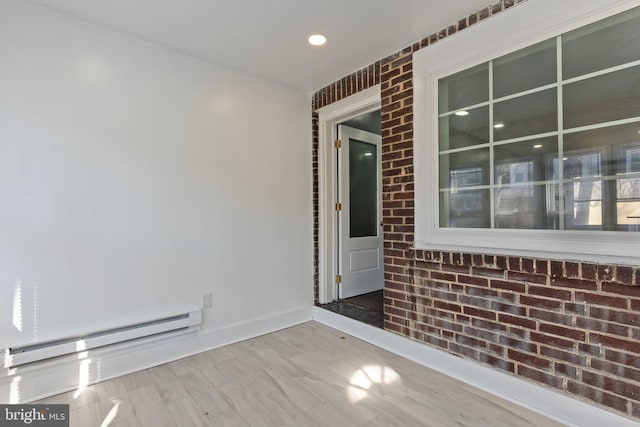 unfurnished room featuring wood finished floors, baseboards, brick wall, and a baseboard radiator